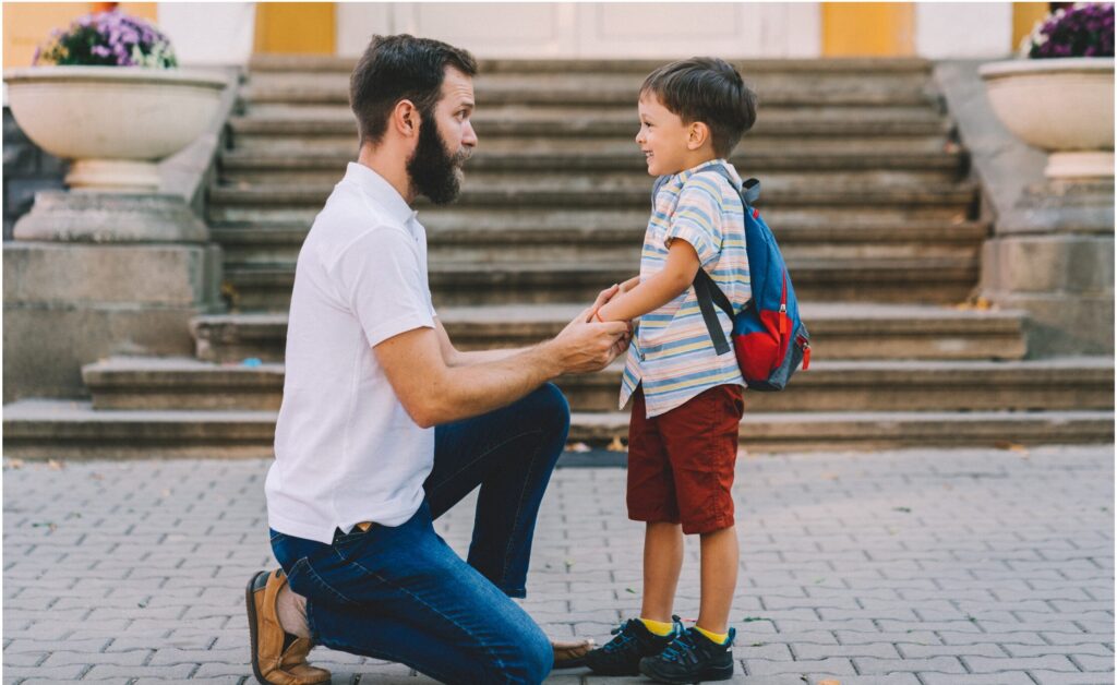 Father kneeling to talk supportively with his young son outside, showing connection and encouragement.
